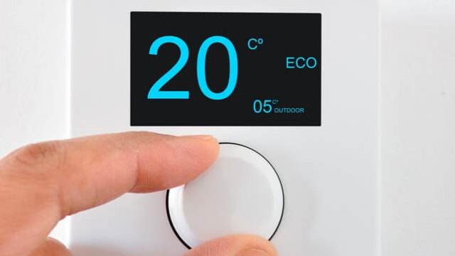 Ein Finger dreht einen weißen Knopf an einem Thermostat. Das Display zeigt 20 Grad Celsius und ECO-Modus an, außen sind es 5 Grad.