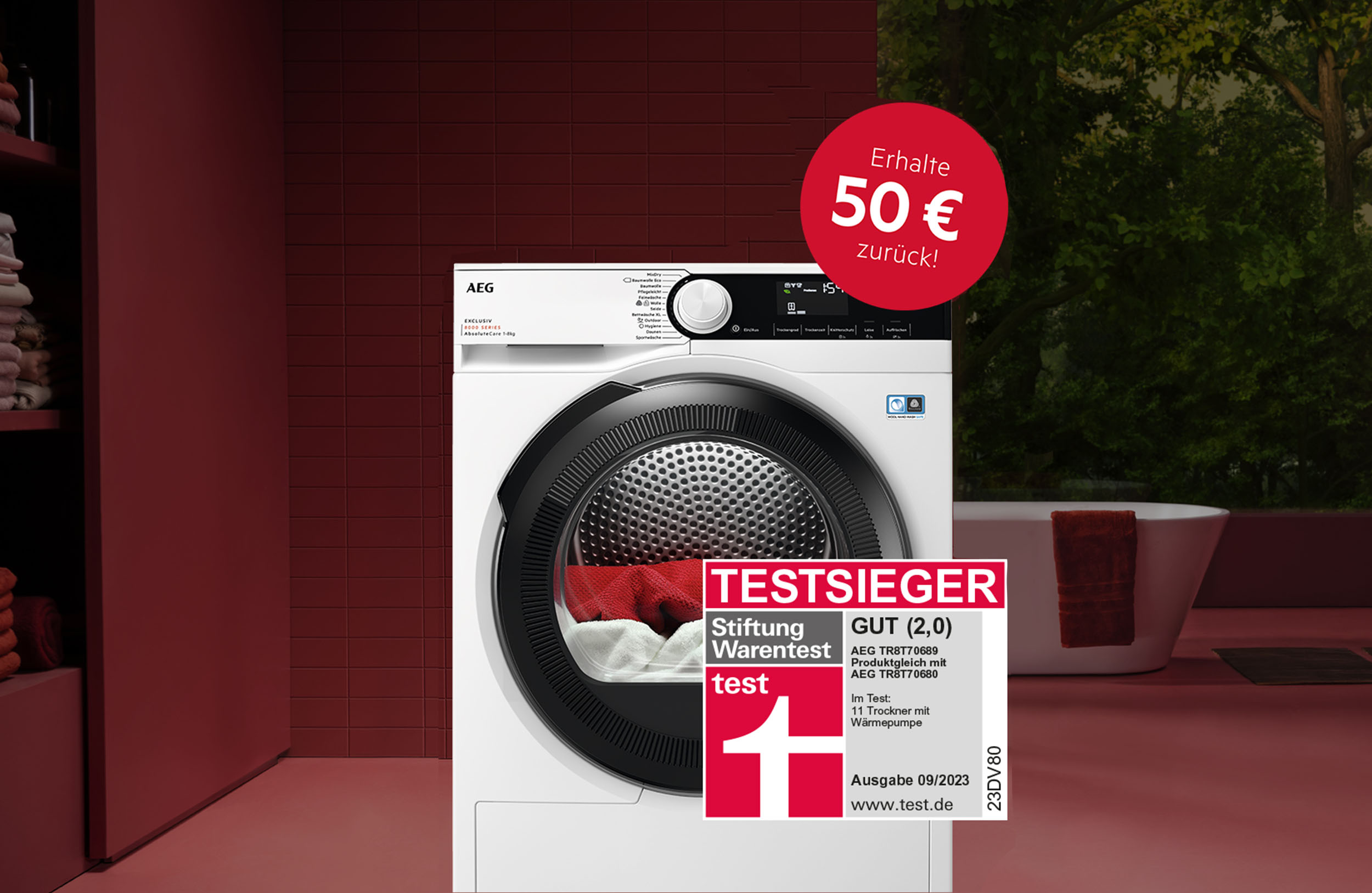 Ein weißer AEG-Trockner steht vor einer roten Wand, daneben ein rotes Regal. Ein roter Kreis mit "50 € zurück!" ist zu sehen. Ein Test-Siegel ist auch da.