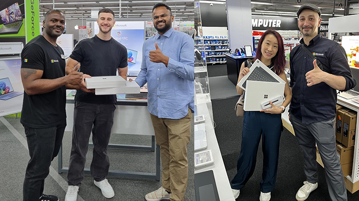 In einem Computergeschäft stehen zwei Gruppen von Leuten und zeigen Daumen hoch, während sie Laptops halten.