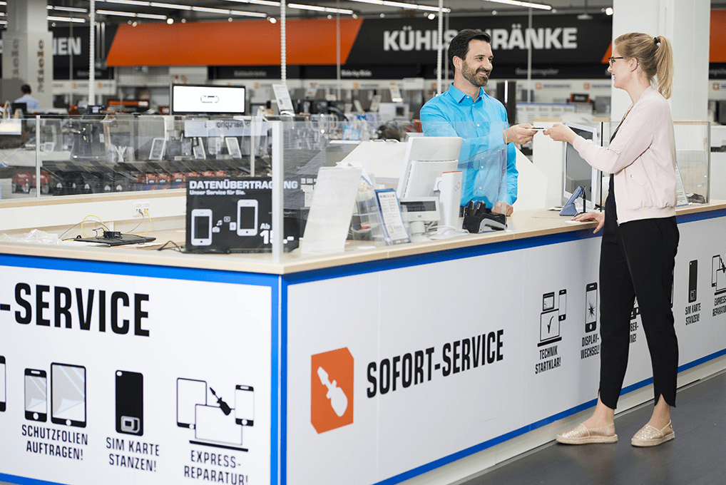 Ein Mann in blauem Hemd übergibt eine Karte an eine Frau an einem Kundendienstschalter in einem Geschäft.