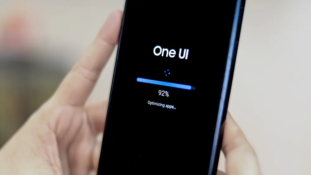 Ein Mobiltelefon in einer Hand zeigt einen Bildschirm mit "One UI", einem blauen Fortschrittsbalken bei 92% und "Apps werden optimiert".