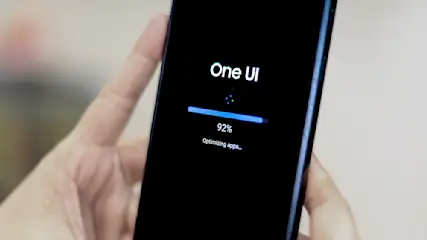 Ein Mobiltelefon in einer Hand zeigt einen Bildschirm mit "One UI", einem blauen Fortschrittsbalken bei 92% und "Apps werden optimiert".