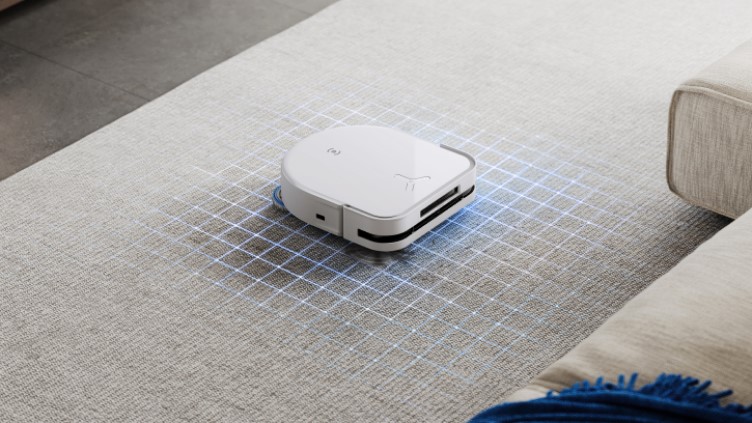 Auf einem Teppich fährt ein weißer Saugroboter, umgeben von einem blauen Gitternetz, nahe eines beigen Sofas.