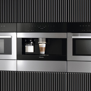 Einbauküchengeräte in Silber mit einer Kaffeemaschine in der Mitte, flankiert von Mikrowellen und einem gestreiften Hintergrund.