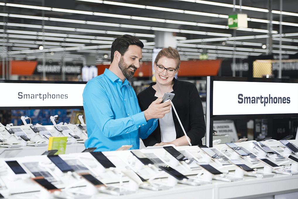 Mann und Frau sehen sich in einem Geschäft Smartphones an, die auf einem weißen Tisch ausgestellt sind.