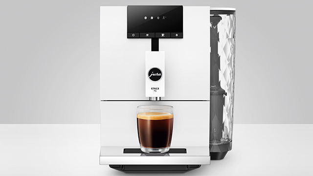 Ein weißer Kaffeevollautomat mit schwarzem Bedienfeld und Wassertank, unter dem Auslauf steht eine Tasse Kaffee.