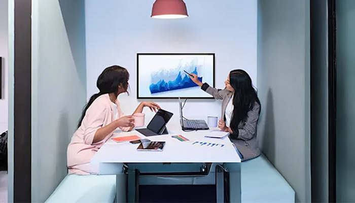 Zwei Personen sitzen an einem Tisch mit Laptops und diskutieren über eine Grafik auf einem Bildschirm.