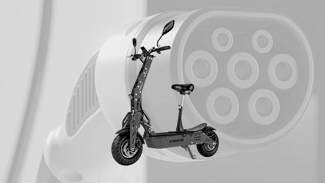 Ein grauer Elektroroller mit Sitz steht vor einem verschwommenen, runden Stecker auf einem hellgrauen Hintergrund.