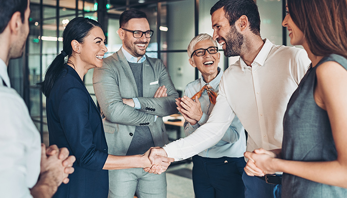Eine Gruppe von Büroangestellten lächelt und schüttelt sich die Hände in einem modernen Büro.