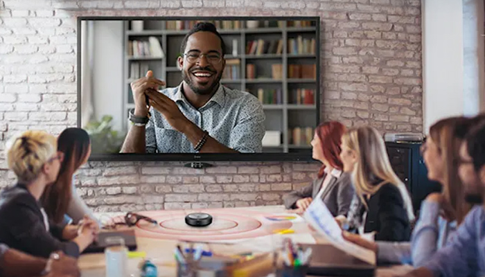 Eine Gruppe von Personen sitzt an einem Tisch und schaut auf einen großen Bildschirm an einer Ziegelwand.