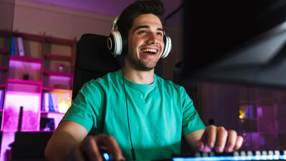 Ein Mann mit Kopfhörern und einem grünen T-Shirt lächelt, während er vor einem Computer mit einer Tastatur sitzt.