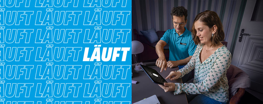 Zwei Personen, Mann und Frau, bedienen ein Tablet; blauer Hintergrund mit dem Wort "LÄUFT" wiederholt.