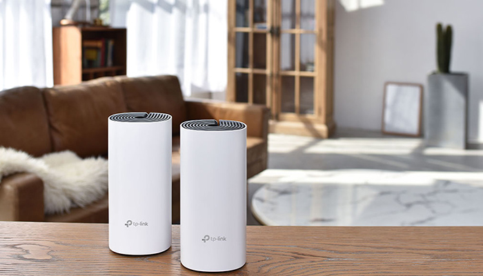 Zwei weiße TP-Link-Geräte stehen auf einem Holztisch. Im Hintergrund ein Sofa, ein Schrank und ein Fenster mit Vorhängen.