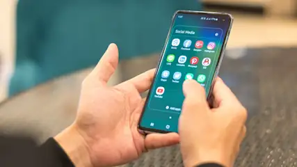 Ein Smartphone mit dem Bildschirm "Social Media" wird von zwei Händen gehalten und bedient. Icons für Apps sind sichtbar.