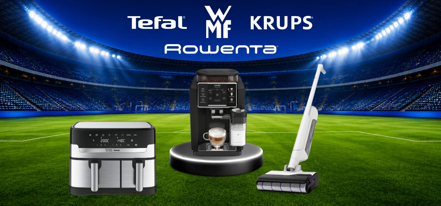 Drei Haushaltsgeräte stehen nebeneinander in einem hell beleuchteten Fußballstadion mit grüner Rasenfläche und gefüllten Tribünen im Hintergrund. Links befindet sich eine Heißluftfritteuse von Tefal, in der Mitte ein schwarzer Kaffeevollautomat mit einer Tasse Kaffee darunter, und rechts ein kabelloser Staubsauger von Rowenta. Unter den Geräten sind die Markenlogos „WMF“, „TEFAL“, „KRUPS“ und „Rowenta“ sichtbar.