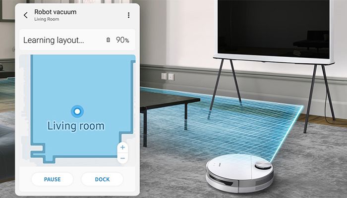 Ein Mobiltelefon zeigt eine Karte eines Wohnzimmers, während ein Roboterstaubsauger den Raum unter einem Fernseher und einem Tisch reinigt.