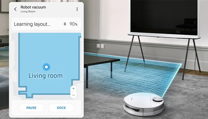 Ein Mobiltelefon zeigt eine Karte eines Wohnzimmers, während ein Roboterstaubsauger den Raum unter einem Fernseher und einem Tisch reinigt.