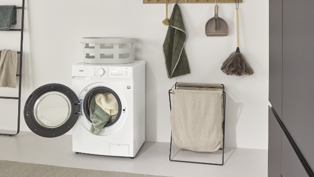 Σύγχρονο πλυντήριο-στεγνωτήριο KOENIC KWDR 8642 A INV σε φωτεινό δωμάτιο πλυντηρίων με ανοιχτή πόρτα και καλάθι πλυντηρίων.