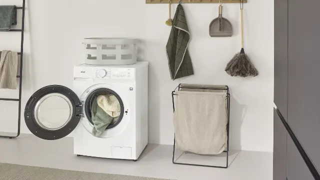 Σύγχρονο πλυντήριο-στεγνωτήριο KOENIC KWDR 8642 A INV σε φωτεινό δωμάτιο πλυντηρίων με ανοιχτή πόρτα και καλάθι πλυντηρίων.