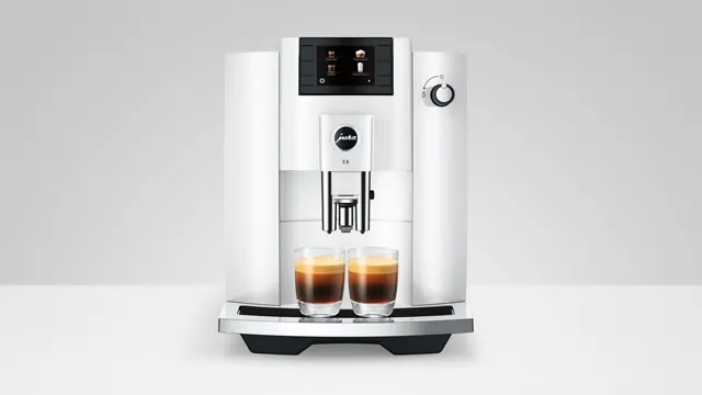 Ein weißer Kaffeevollautomat mit zwei Gläsern braunem Kaffee steht auf einer weißen Oberfläche vor einem hellgrauen Hintergrund.