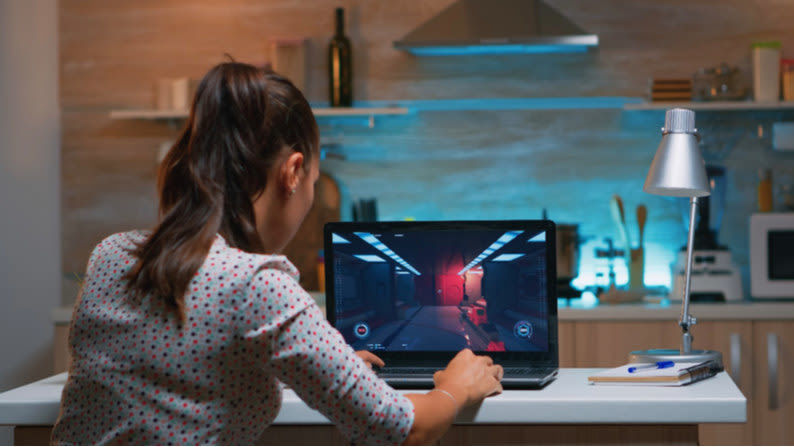 Eine Frau sitzt am Laptop und spielt ein PC Spiel.