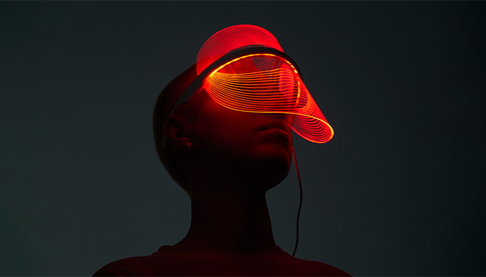 Ein Mensch trägt ein rotes LED-Visier mit einem schwarzen Kabel vor einem dunklen Hintergrund.