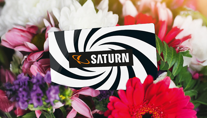 MediaMarkt Geschenkkarte mit rotem Wirbel-Design liegt zwischen bunten Blumen, ideal als Geschenk.
