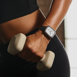 Sportliche Person mit Smartwatch am Handgelenk, die in Trainingskleidung eine helle Kurzhantel fest in der Hand hält.