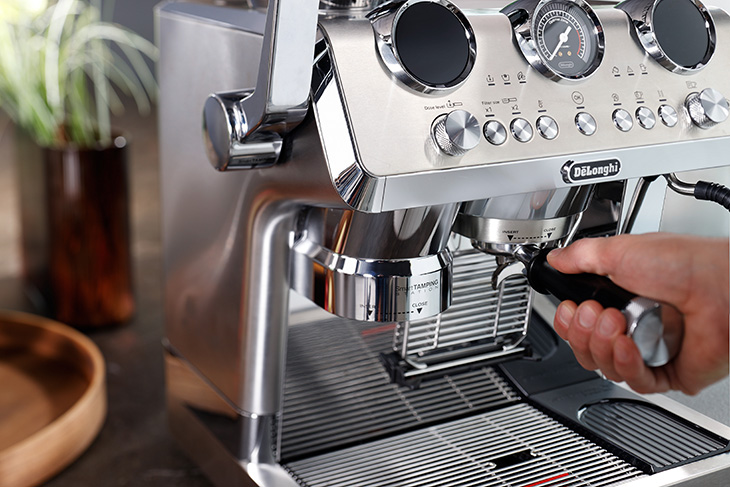 Moderne Siebträgermaschine auf einer Kücheninsel, umgeben von frisch zubereiteten Kaffees in einem hellen, stilvollen Wohnraum.