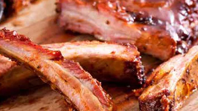 Nahaufnahme von gegrillten Spareribs auf einem hellbraunen Holzbrett, die mit einer dunklen Soße überzogen sind.