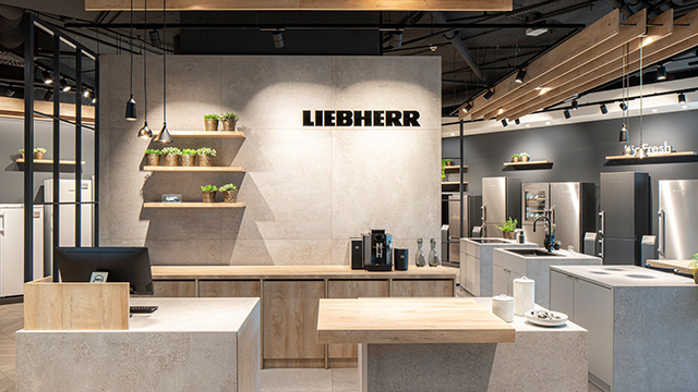 Innenraum eines Küchenausstellungsraums mit Geräten, Arbeitsplatten und dem Schriftzug "LIEBHERR" an der Wand.