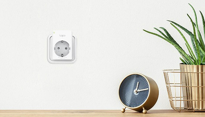 Nahaufnahme einer Steckdose an einer Wand, einer Uhr und einer Pflanze in einem goldenen Übertopf.