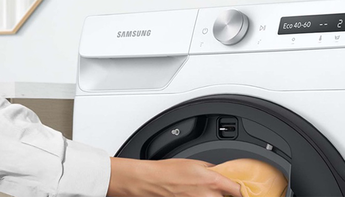 Eine weiße Samsung-Waschmaschine mit einer Hand, die ein beiges Kleidungsstück hineinlegt. Das Display zeigt "Eco 40-60".