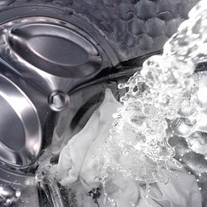 Wasser fließt in eine silberfarbene Waschmaschine mit weißer Wäsche im Inneren.