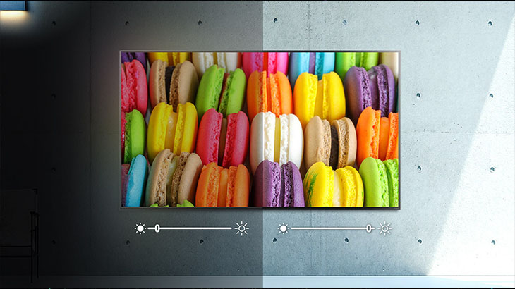 Ein Bildschirm zeigt Macarons in vielen Farben auf einer Betonwand. Helligkeitsregler sind unten sichtbar.