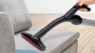 Ein Staubsauger reinigt das Polster eines Sofas.