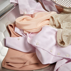 Helle und pastellfarbene Kleidungsstücke liegen in einer silbernen Trommel, möglicherweise einer Waschmaschine oder einem Trockner.