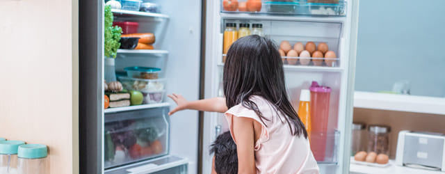 Kind schaut in offenen Kühlschrank voller Lebensmittel.