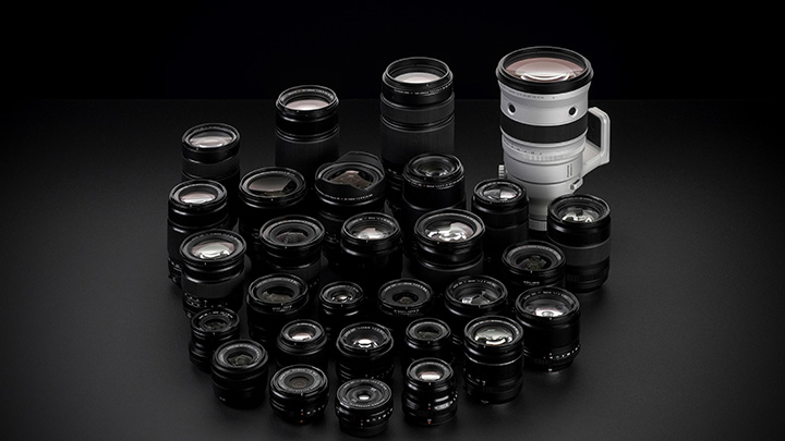 Auf schwarzem Grund sind zahlreiche schwarze Kameraobjektive unterschiedlicher Größe und ein größeres, weißes Objektiv zu sehen.