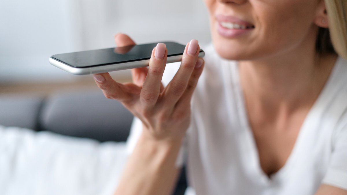 Eine Frau hält ein schwarzes Smartphone in der Hand, während sie ein weißes T-Shirt trägt.