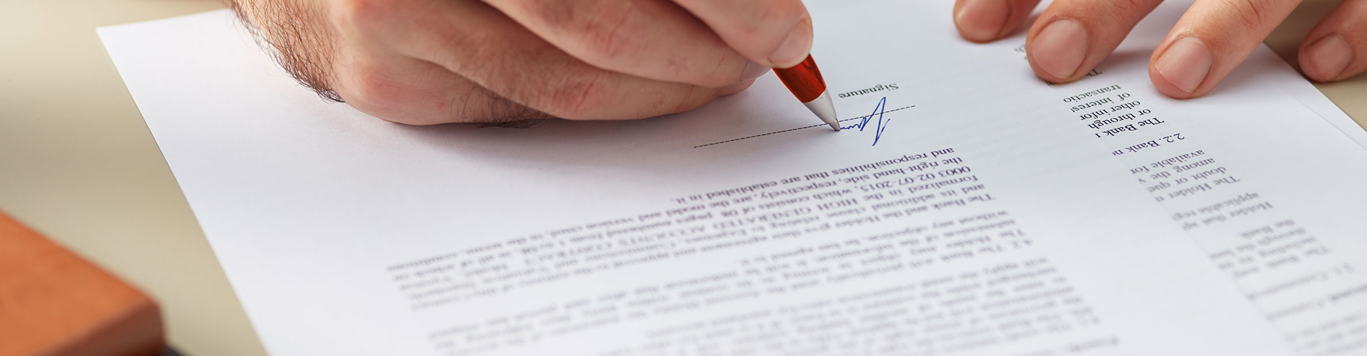Eine Person unterschreibt ein Dokument mit rotem Stift auf einem weißen Blatt Papier mit Text.