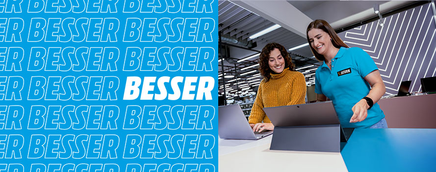 Eine Frau im gelben Pullover und eine im blauen Poloshirt stehen vor Laptops an einem Verkaufstisch. Im Hintergrund sind Regale.