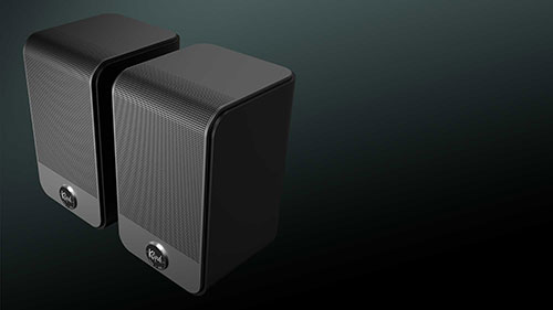 Due altoparlanti rettangolari grigi con bordi curvi su sfondo scuro. L'altoparlante di destra ha una griglia verticale.