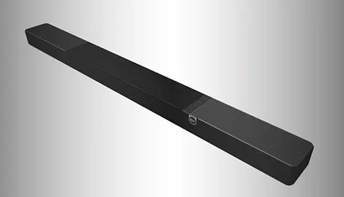 Lunga soundbar nera su sfondo grigio sfumato. La soundbar è rettangolare con estremità smussate e dettaglio circolare.
