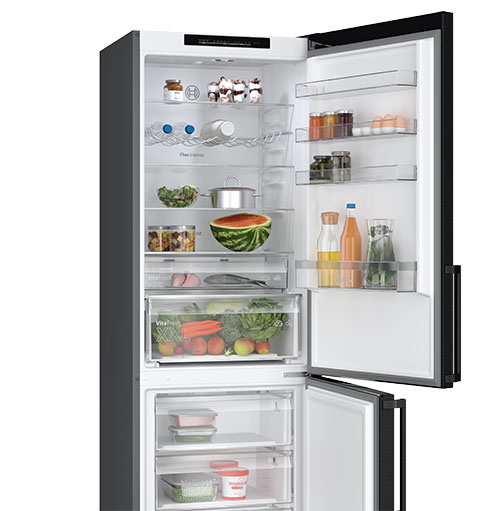 Frigorifero bianco e nero aperto, pieno di cibo. Si vedono frutta, verdura, bevande e contenitori.