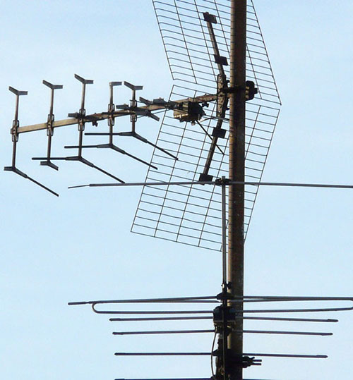 Antenna TV metallica su palo, con elementi orizzontali e griglia, contro un cielo azzurro.
