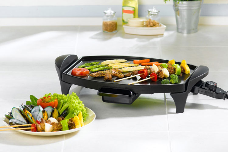 Griglia elettrica con spiedini di verdure e carne. Un piatto di cozze e verdure � a sinistra. Sullo sfondo, utensili da cucina.