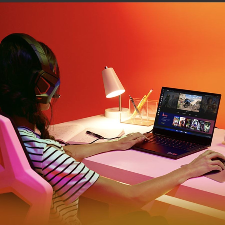 Ragazza con cuffie usa un laptop su una scrivania rosa con lampada e porta penne. Sfondo arancione.