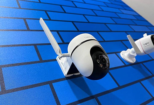 Due telecamere di sicurezza bianche montate su una parete blu con motivo a mattoni scuri.