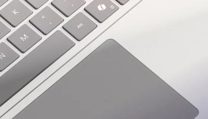 Tastiera grigia con lettere bianche e trackpad grigio su sfondo bianco. Si vedono i tasti Alt, M, N e K.
